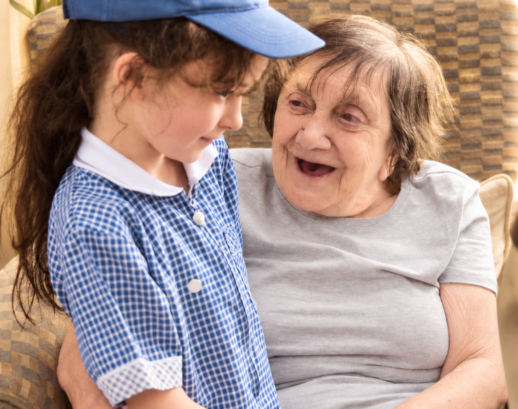 A child in a school uniform and an older woman laughing together on a sofa at an Intergenerational Music Making session